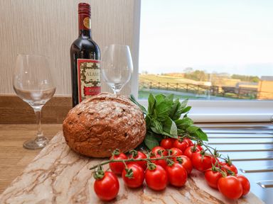 A loaf of bread red tomatoes green basil leaves two wine glasses and a bottle of red wine on a kitchen countertop with a window view at Cherry Blossom Lodge in Whitby