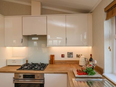 A kitchen with a gas stove oven wooden countertop bread box cutting board with bread tomatoes basil wine bottle and glasses at Cherry Blossom Lodge in Whitby