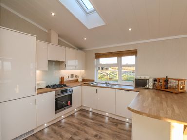 A kitchen with white cabinets wooden countertops a gas stove oven microwave and a window at Cherry Blossom Lodge in Whitby