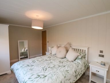 A bedroom with a bed with green leaf pattern bedding pillows a side table a wardrobe a mirror and a ceiling light at Cherry Blossom Lodge in Whitby