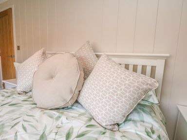 A bed with patterned cushions and leaf print bedding in a bedroom at Cherry Blossom Lodge in Whitby