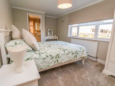 A bedroom with a bed with leaf patterned bedding, bedside table with a vase, dressing table with mirror and window at Cherry Blossom Lodge in Whitby