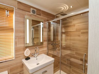 A bathroom with a sink and mirror next to a glass shower enclosure with a rain showerhead at Cherry Blossom Lodge in Whitby