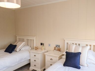 A bedroom with two single beds white bedside tables and cushions at Cherry Blossom Lodge in Whitby
