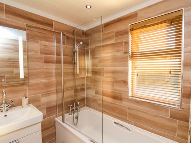 A bathroom with a bathtub shower combination a sink with a faucet and soap dispenser and a window with wooden blinds at Cherry Blossom Lodge in Whitby