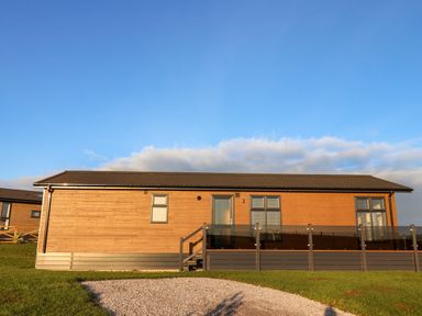 A wooden single-story house with glass railing on the deck and gravel path in front at Cherry Blossom Lodge in Whitby