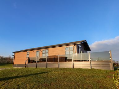 A single story wooden house with glass railing on a grassy slope at Cherry Blossom Lodge in Whitby
