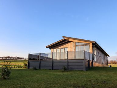 A wooden cabin with glass balcony on a grassy lawn under a clear blue sky at Holly Lodge in Whitby