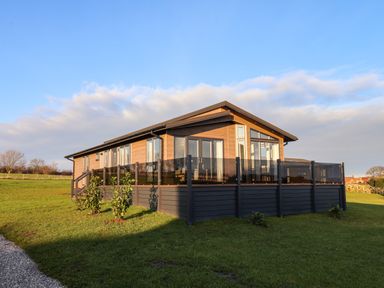 A single story wooden house with glass balcony panels surrounded by grass at Holly Lodge in Whitby