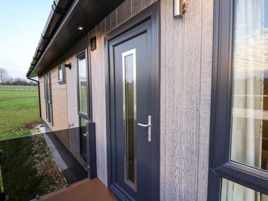 An exterior view of a building with a door and windows on a wooden deck with glass railing at Holly Lodge Whitby