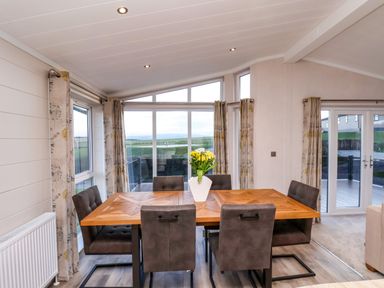 A dining room with a wooden table and six chairs and a vase with flowers on the table at Holly Lodge in Whitby