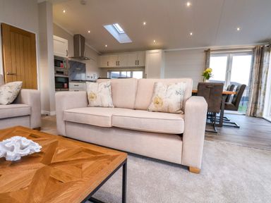 A living room with a beige sofa and wooden coffee table next to a kitchen and dining area at Holly Lodge in Whitby