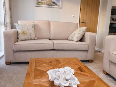 A beige sofa with two floral cushions and a wooden coffee table with a white decorative item in a living room at Holly Lodge in Whitby