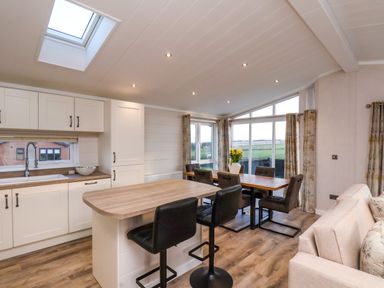 A kitchen and dining area with a wooden island and black chairs and a dining table with six chairs and windows showing a green field at Holly Lodge in Whitby