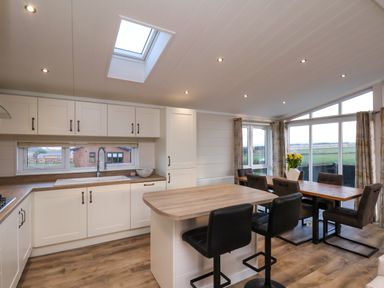 A kitchen with white cabinets an island with two black stools and a dining area with a wooden table and six chairs at Holly Lodge in Whitby