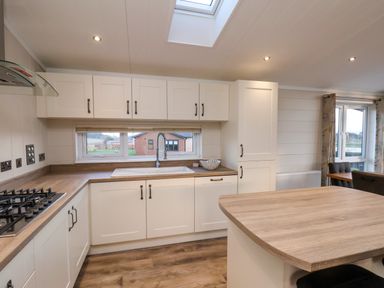 A kitchen with wooden countertops white cabinets a gas stove a sink under a window and a central island at Holly Lodge in Whitby