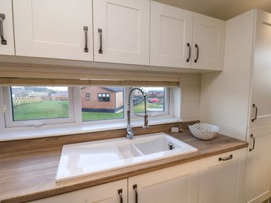 A kitchen sink with a faucet under a window and cabinets above and below the counter at Holly Lodge in Whitby