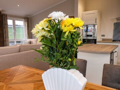 A bouquet of yellow and white flowers in a white vase on a wooden table in a kitchen and living area at Holly Lodge in Whitby