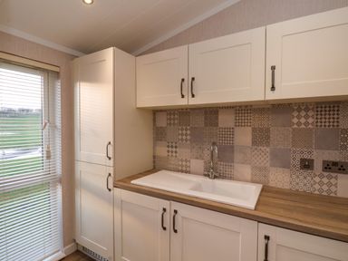 A kitchen with white cabinets a double sink and patterned tile backsplash at Holly Lodge in Whitby