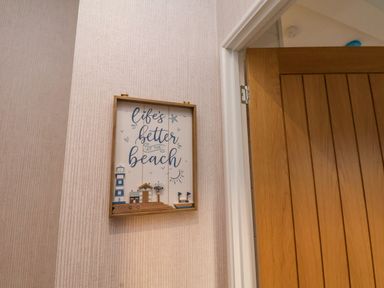 A wall with a framed beach-themed sign next to a wooden door at Holly Lodge in Whitby
