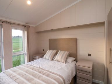 A bedroom with a bed with pillows and a striped blanket two bedside tables and a window showing green fields at Holly Lodge in Whitby