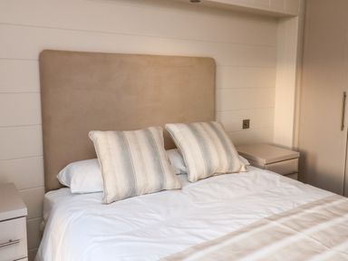 A bedroom with a bed two striped pillows white bedding beige headboard and bedside tables at Holly Lodge in Whitby
