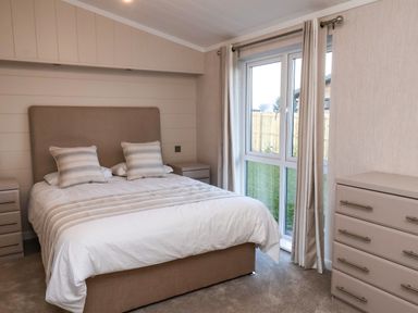 A bedroom with a bed two pillows two bedside tables and a dresser near a window with curtains at Holly Lodge Whitby