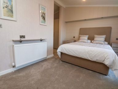 A bedroom with a double bed two pillows a carpeted floor two framed paintings a radiator and bedside cabinets at Holly Lodge in Whitby