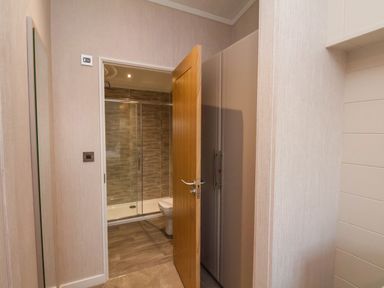 A hallway with an open wooden door leading to a bathroom with a glass shower enclosure and a toilet at Holly Lodge in Whitby