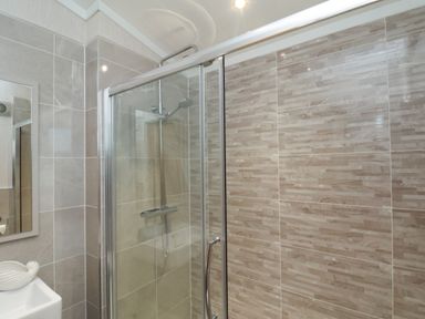 A bathroom with a glass shower enclosure and tiled walls at Holly Lodge in Whitby
