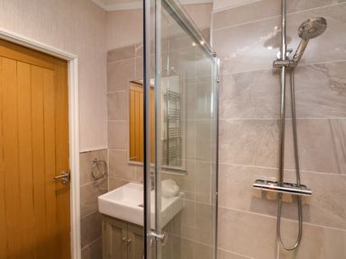 A bathroom with a wooden door a white sink and a glass-enclosed shower at Holly Lodge in Whitby