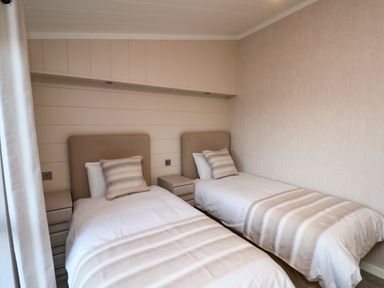 A bedroom with two single beds each with a pillow and a bedside table between at Holly Lodge Whitby