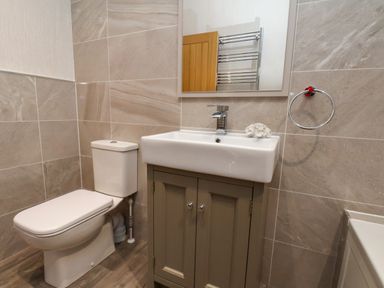 A bathroom with a toilet sink with cabinet and mirror towel ring on a tiled wall at Holly Lodge in Whitby