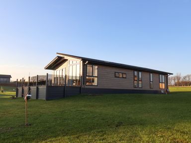 A single story house with large windows and a glass enclosed porch on a grassy hill at Holly Lodge in Whitby