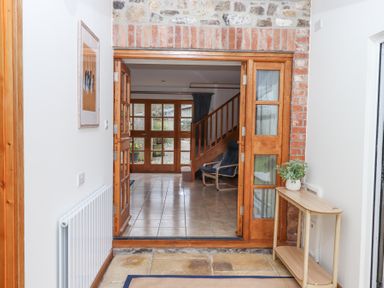 A hallway with wooden doors and a small wooden table with a plant leading to a room with tiled flooring and a staircase at The Old Coach House Little Dunley Cottages near Bovey Tracey