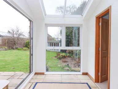 A room with large windows overlooking a garden with grass and plants at The Old Coach House Little Dunley Cottages near Bovey Tracey
