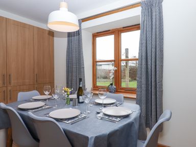 A dining area with a table set for six people near a window with curtains at The Old Coach House in Little Dunley Cottages near Bovey Tracey