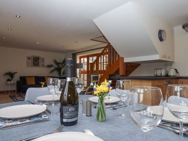 A dining table set with plates glasses and prosecco bottle in an open plan kitchen and living area at The Old Coach House Little Dunley Cottages near Bovey Tracey