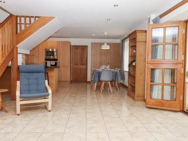 A kitchen and dining area with wooden cabinets a blue cushioned chair and a table set for dining at The Old Coach House Little Dunley Cottages near Bovey Tracey