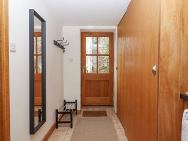 A hallway with a wooden door with glass panels a black-framed mirror a wall-mounted coat rack and a shoe rack at The Old Coach House Little Dunley Cottages near Bovey Tracey