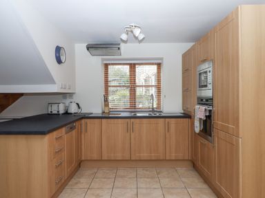 A kitchen with wooden cabinets a black countertop appliances and a window with blinds at The Old Coach House Little Dunley Cottages near Bovey Tracey