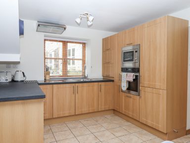 A kitchen with wooden cabinets a window with blinds a sink microwave oven toaster and kettle at The Old Coach House in Little Dunley Cottages near Bovey Tracey