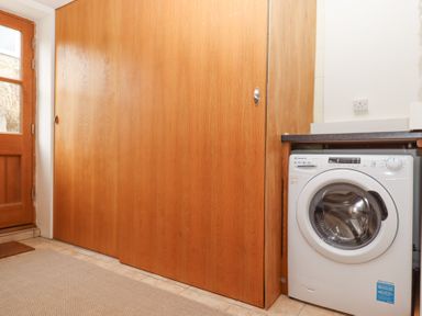 A laundry room with a washing machine next to wooden sliding doors and a wooden door at The Old Coach House Little Dunley Cottages near Bovey Tracey