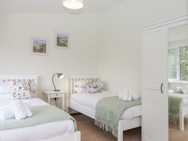 A bedroom with two single beds a nightstand with lamp and a wardrobe with mirror at The Old Coach House Little Dunley Cottages near Bovey Tracey