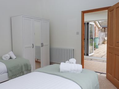 A bedroom with two single beds and a white wardrobe near a door leading outside at The Old Coach House Little Dunley Cottages near Bovey Tracey