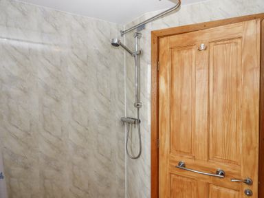 A bathroom with a mounted shower head and a wooden door with a metal handle at The Old Coach House Little Dunley Cottages near Bovey Tracey