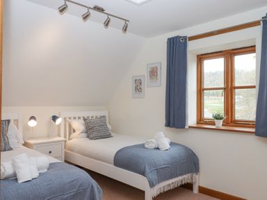 A bedroom with two single beds and a window with blue curtains at The Old Coach House in Little Dunley Cottages near Bovey Tracey