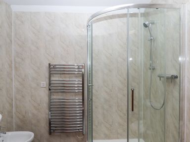 A bathroom with a glass shower enclosure and a wall-mounted chrome towel radiator at The Old Coach House in Little Dunley Cottages near Bovey Tracey