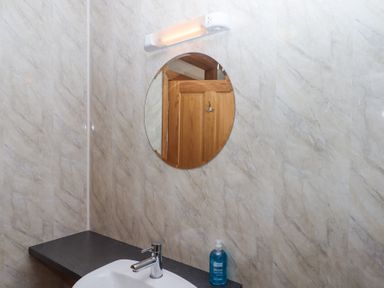 A bathroom sink with a faucet and blue hand wash bottle under a round mirror with a light above at The Old Coach House Little Dunley Cottages near Bovey Tracey