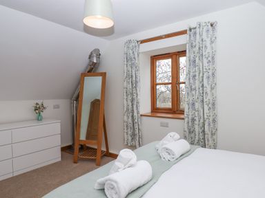 A bedroom with a bed and rolled towels a floor mirror a window with floral curtains and a white chest of drawers at The Old Coach House Little Dunley Cottages near Bovey Tracey